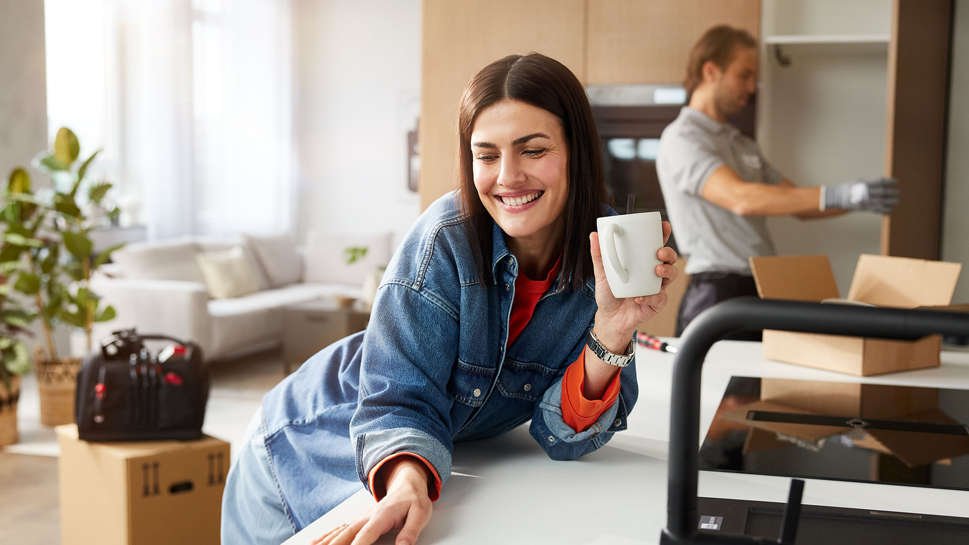 Frau steht zufrieden in ihrer Küche und genießt dabei einen Kaffee.